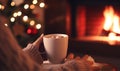 A mug of steaming hot chocolate or coffee enjoyed by the Christmas fireplace as a woman relaxes by the warm fire, embodying the