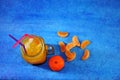 A mug of tangerine juice with ice and straws is in a heap of citrus slices on a blue background Royalty Free Stock Photo