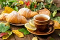 Mug of tea with lemon, croissant, autumn fall leaves on wooden background. Cozy home breakfast, autumn hygge style, comfort