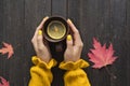 Mug of tea with lemon in a female hand. Wooden background, autumn leaves. Top view