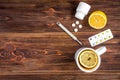 Mug of tea with lemon, lemon, thermometer and pills on wooden background. Cold treatment. Flu season