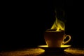 A mug with a warm drink and curly steam rising up, illuminated in red-yellow, orange on a black background