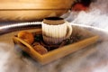 A mug of warm tea with pieces of manadarines on a wooden tray in the smoke