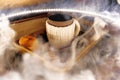 A mug of warm tea with pieces of manadarines on a wooden tray in the smoke