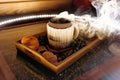 A mug of warm tea with pieces of manadarines on a wooden tray in the smoke