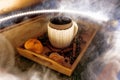 A mug of warm tea with pieces of manadarines on a wooden tray in the smoke