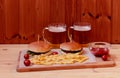 Mugs of beer, burgers and fried potatoes on wooden table. Selective focus