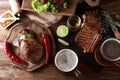 Mugs of delicious beer with steaks and spices on wooden table Royalty Free Stock Photo