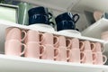 Mugs on shelf on a shelf in retail gift store. Pink and dark blue coffee mugs on shelf in kitchen. Stack of ceramic cups Royalty Free Stock Photo