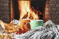 Mugs of tea or coffee, woolen thing and viburnum berries before cozy fireplace, in country house, autumn or winter holidays