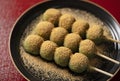 Mugwort dumplings covered with soybean flour, served on a black plate placed on a red tray