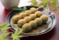 Mugwort-flavored rice dumpling covered with soybean flour and green tea served on a black plate placed on a red tray