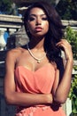 Mulatto girl wears elegant coral dress with bijou ,posing beside antic palace