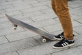 Skater legs wearing black sneakers by Adidas waiting with skate board in the street