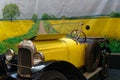 Old car in front of a photo of yellow fields