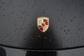 Closeup of rain drops on porsche logo on a black car parked in the street