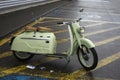 Profile view of green vintage scooter parked in the street by rainy day