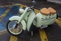 Profile view of green vintage scooter parked in the street by rainy day