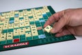 Hand of woman playing with plastic letters to forming a word on Scrabble board game  on white tableword on Scrabble board Royalty Free Stock Photo