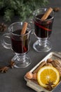 Mulled wine in glasses at black background. Fir wreath, tray with orange, cinnamon, nuts, cone and spices near