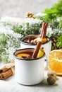 Mulled wine in white metal mugs with cinnamon, spices and orange with fir tree and christmas lights - traditional drink on winter Royalty Free Stock Photo