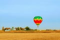 A multi-colored balloon is flying over a field in the sky near a