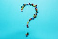 Multi-colored children`s beads, scattered on a blue background, question mark