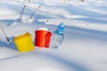 Multi-colored coffee cups and a plastic bottle stick out of the snow. Household waste environmental pollution concept Royalty Free Stock Photo