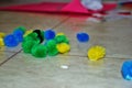 Multi colored cotton pompoms, glue, glue sticks, construction paper, and scissors covering a linoleum floor during arts and crafts