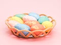 Multi-colored decorative eggs in pastel colors lie in a wicker plastic basket on a light pink. Royalty Free Stock Photo