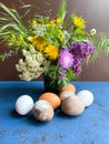 Multi-colored Easter eggs and bright wild flowers in a decorative vase, against a background of an abstract surface. Royalty Free Stock Photo