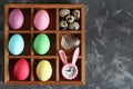 Multi-colored Easter eggs and a rabbit-shaped clock in wooden cells on a concrete background. Top view