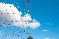 Multi-colored flags against a blue sky with clouds and a dome of a church