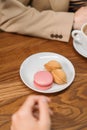 Multi-colored french macaron cookies with different fillings on plates, a female hand holds a bitten macaroon. Close-up shot