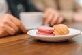 Multi-colored french macaron cookies with different fillings on plates, a female hand holds a bitten macaroon. Close-up shot