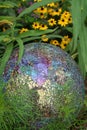 Colorful mosaic glass gazing ball sits amidst a summer flower garden