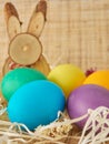 Multi colored painted eggs on wooden background with wooden rabbit. Happy Easter concept, copy space. Royalty Free Stock Photo