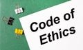 Multi-colored paper clips and a sheet of paper with the text CODE OF ETHICS on a green notepad