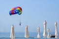 Multi-colored parachute with a man on the background of the sea and white closed beach umbrellas. The completion of the flight by