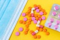 Multi-colored pills and a blue disposable mask on a bright yellow background, top view. Medication for the disease. Drugs from cor