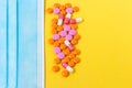 Multi-colored pills and a blue disposable mask on a bright yellow background, top view. Medication for the disease. Drugs from cor