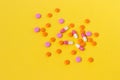 Multi-colored pills are scattered on a bright yellow background, top view. Medication for the disease for patients. Dose drugs and