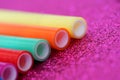 Multi-colored plastic tubes on a bright, sparkling lilac surface. Close-up. Manual for teaching preschoolers. Shallow depth of