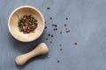 Multi-colored red green black peppercorns in a wooden mortar with a pestle and scattered around on a ultimate gray Royalty Free Stock Photo