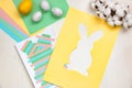 Multi-colored sheets, scissors, glue, Easter eggs, cut out rabbit pattern on a yellow sheet of paper on a light table. DIY concept Royalty Free Stock Photo