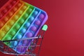 The multi-colored toy is a popit simple dimple anti-stress in a basket of stroller shopping carts on a red background with a place