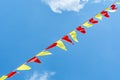 Multi colored triangular flags develop on the background of blue sky. Colorful fairground flags