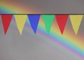 Multi Colored Triangular Flags Hanging in the Sky at an Outdoor against the backdrop of a rainbow. Royalty Free Stock Photo