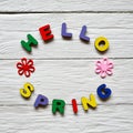 Multi-colored wooden letters making up the words Hello spring and multi-colored wooden flowers on a white wooden background.