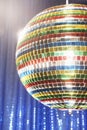 Multi-coloured disco ball in front of blue stage curtain cropped